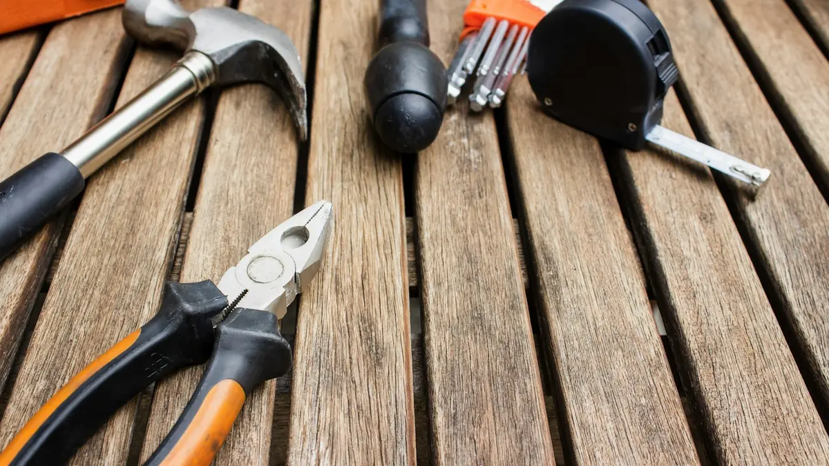 A selection of tools including pliers, hammer, screwdriver set, and a measuring tape on wooden surface.