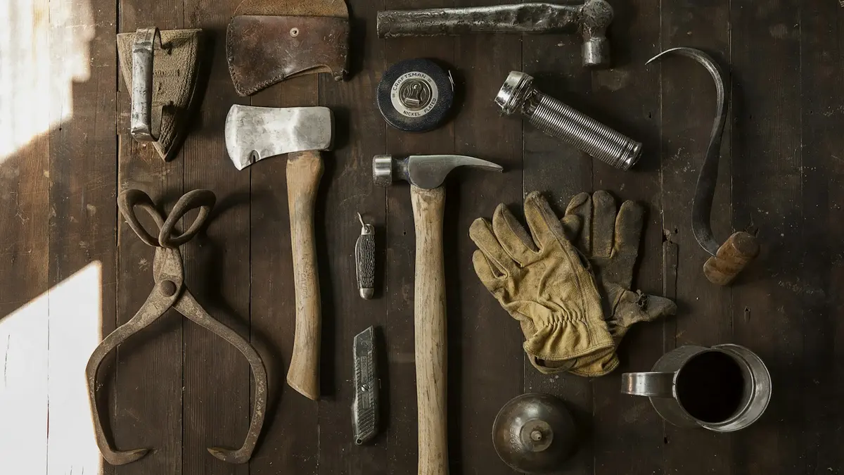 Assorted hand tools including hammers, axes, gloves, and a measuring tape on a wooden surface.