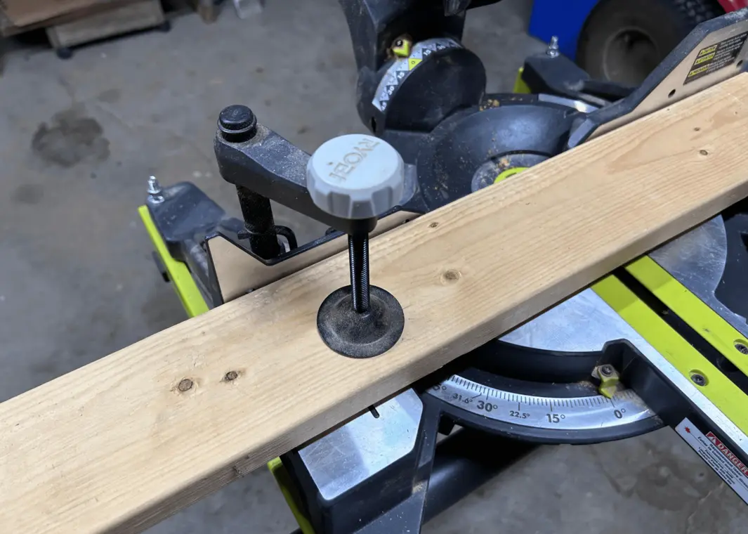 Miter saw with a wood board secured in place by a clamp.