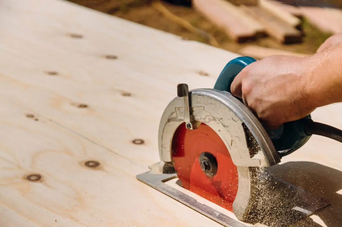 A person using a circular saw to cut plywood on a workbench.