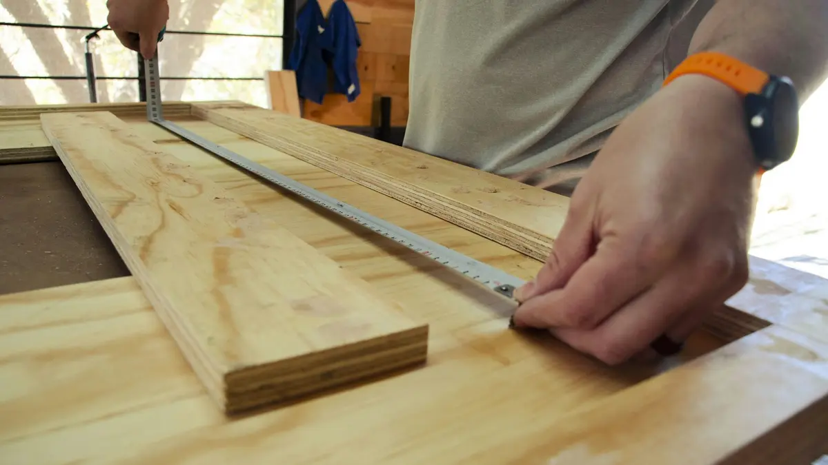A person measuring and marking wood for a rip cut with a straight edge.